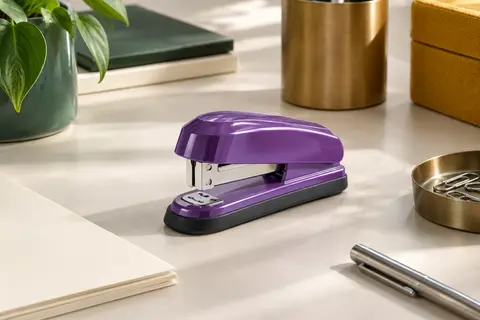 Agrafeuse de bureau violette à base en caoutchouc posée sur un bureau clair avec du papier ivoire.
