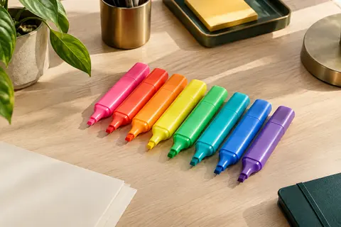 Huit surligneurs en plastique aux couleurs vives assorties, avec des pointes biseautées, posés sur un bureau rangé.