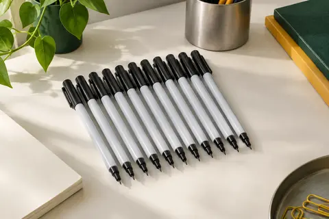 Douze marqueurs Sharpie noirs à pointe fine disposés sur un bureau rangé avec du papier ivoire.